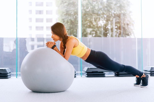Beautiful young Asian woman training pilates, yoga plank at gym with exercise ball