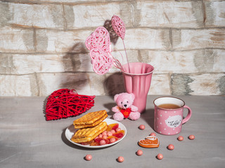 Greeting Card Happy Valentine's Day. Pink dishes, decor and Viennese waffles with a mug of tea.