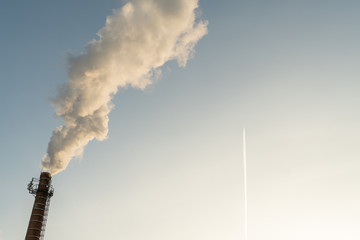 The factory produces acrid smoke from the chimney. In the clear sky flying plane.