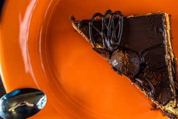 A piece of chocolate cake on an orange plate photographed close-up.