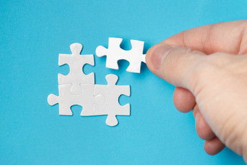 Hand inserting missing piece of a blank puzzle on blue background
