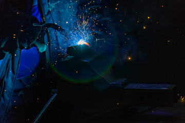 Welder in gloves welds a metal part in the factory. Glare of spark and smoke during the wizard