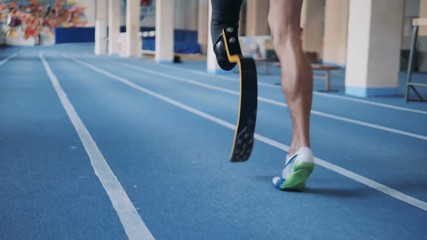 One man with bionic leg training on a running track, back view. - Powered by Adobe