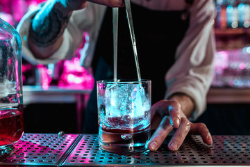 Expert barman is making cocktail at night club or bar. Glass of fiery cocktail on the bar counter against the background of bartenders hands with fire. Barman day concept