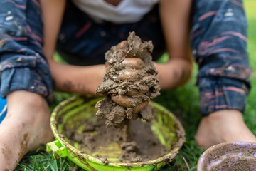 Closeup of toddler boy sitting barefoot in a green grass playing with mud