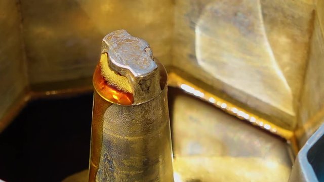 Extreme close up of the process of orange-coloured rose water brewing out of a brassy metal apparatus