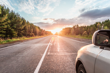 The car moves on the road through the woods during sunset. Photo taken outside the car from the...