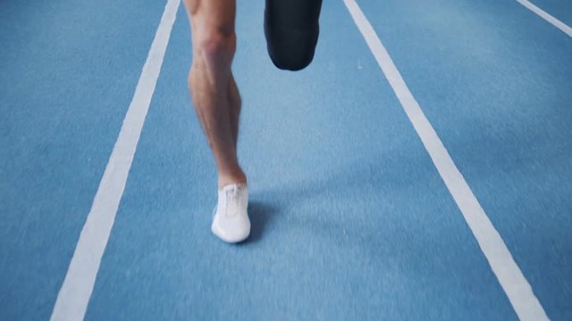 Man with leg prosthesis running on a training track, close up.