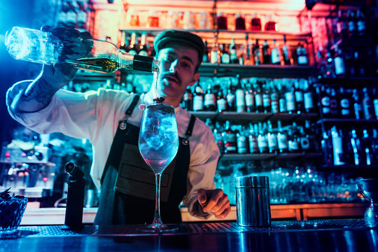 Expert barman is making cocktail at night club or bar. Glass of fiery cocktail on the bar counter against the background of bartenders hands with fire. Barman day concept