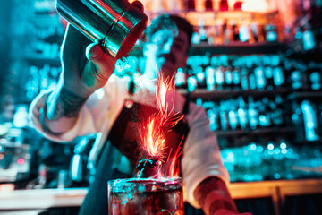 Glass of fiery cocktail on the bar counter against the background of bartenders hands with fire....