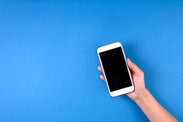 Hand touching smartphone screen on blue background. Mock-up. Top view. Copy space