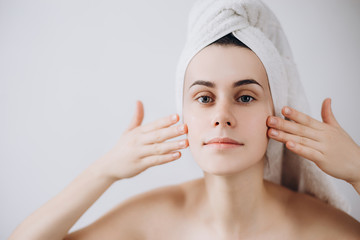 A young beautiful girl after a shower with a towel on her head apply a cleansing mask on her face....