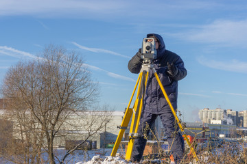 Surveyor conducts a topographical survey in winter for cadastral work at a construction site