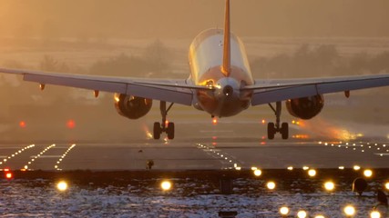 Commercial Jet Airplane Landing in airport runway at sunset in Winter. Slow Pan. - Powered by Adobe