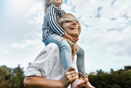 Image of cute little funny daughter on a piggy back ride with her happy mother. Loving woman and her little girl playing in the park. Mom and kid have fun outside. Good relationship. Mother's day
