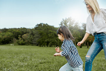 Happy pretty little girl playing catch me with her mother on green grass in the park. Loving beautiful woman and her daughter spending time together. Mom and kid has fun. Mother's day