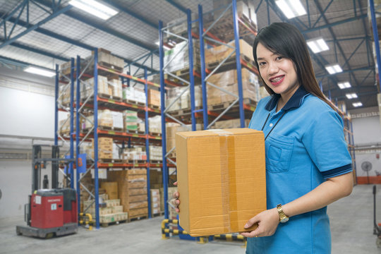 Pretty worker carrying box in the warehouse (ฺBlur background) ,Professional asian delivery woman bring the cardboard box in the distribution warehouse (ฺBlur background)