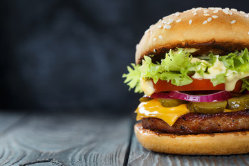 Close-up of delicious fresh home made burger with lettuce, cheese, onion and tomato on a dark...