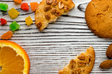 Round orange biscuits with colorful candied fruits and a slice of juicy orange lying on a wooden table