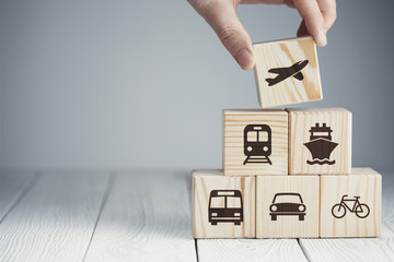 Hand putting a wooden cube with airplane icon on top of cubes with different kinds of transport icons, on neutral background