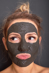 Portrait of a naughty girl with a black clay mask on her face