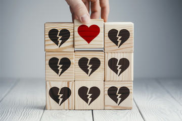 Hand putting the cube with a red heart symbol, which is opposite to black broken hearts on other wooden cubes