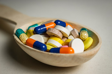 Many colored tablets in a wooden spoon on a white table