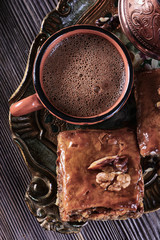 A cup of freshly brewed coffee next to a cezve and baklava on a wooden vintage tray and on a wooden background, vertical, top view