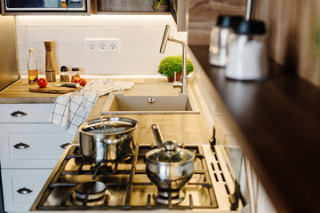 Cooking food on modern kitchen with steel oven, pots, knife on wooden cutting board with vegetables, pepper, spices,oil on wooden tabletop. Home food. Stylish kitchen furniture in grey color