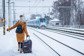 Woman with luggage is running at leaving train at railway station during blizzard. I am late !