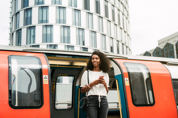Black woman using mobile phone at london underground - obrazy, fototapety, plakaty