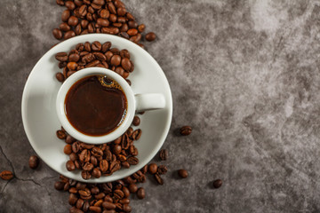 White cup with black coffee and grains of coffee on a background of gray stone. View from above. Place for text.