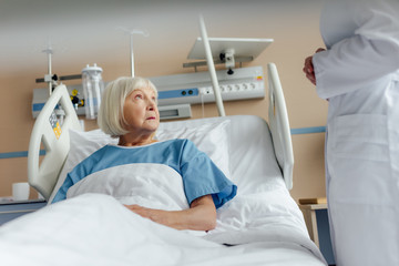 doctor consulting upset senior woman lying in hospital bed