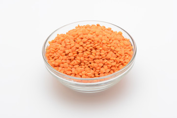 Lentejas naranjas crudas en un bol de cristal sobre fondo blanco