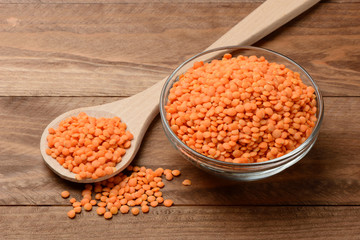 Lentejas naranjas crudas en un bol y una cuchara en la mesa de madera
