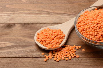 Lentejas naranjas crudas en un bol y una cuchara en la mesa de madera