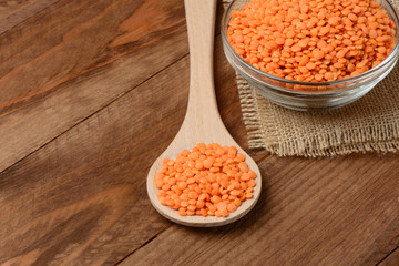 Lentejas naranjas crudas en un bol y una cuchara en la mesa de madera