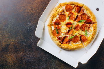 Pizza in a cardboard box against a dark background. Space for text. View from above. Pizza delivery. Pizza menu.