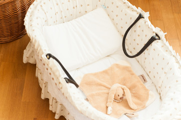 view from above of baby cot with white bed sheet and teddy indoors, inside warm wooden home
