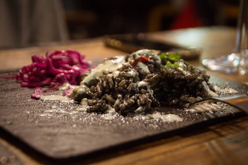 Black rice with white sauce, red cabbage and greens on a black square plate