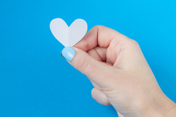 hand holding a white heart on a blue background. Background for Valentine's day.the eighth of March,place for text
