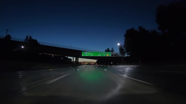Dawn driving on wet pavement below Pasadena 210 freeway overhead sign near Los Angeles in Southern California.