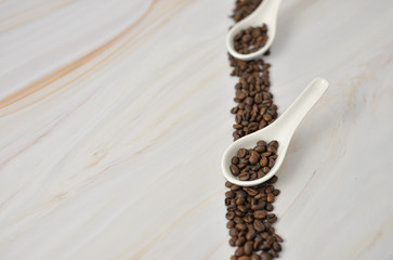 Coffee beans on marble background in white spoons with copy space