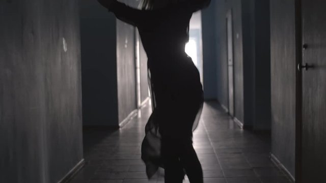 Silhouette of woman in tulle dress dancing and spinning around while going along hallway