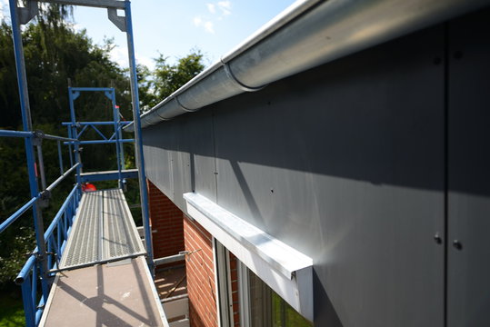 Dach Baustelle Flachdach Renovierung. Schwarzer Traufkasten mit neuer Zink Dachrinne. Ansicht aus oberster Lage des Ger&uuml;stes.