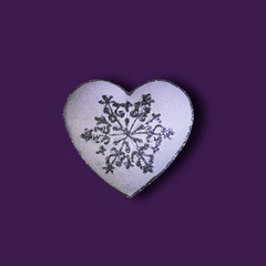 White heart with glitter silver snowfalake isolated on a purple background. Saint Valentine's Day concept. Flat lay. Top view.