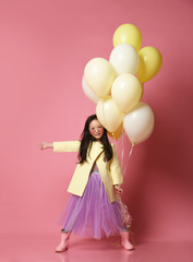 Little Korean baby girl in yellow fashion jacket and purple dress with balloons thumb up celebrate happy smiling