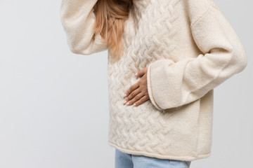 Cropped shot of woman in white sweater suffering from abdominal pain, having menstruation pain, feels bad, side view. Menstrual period, gynecology, gastritis, healthcare, medical concept. Copy space.