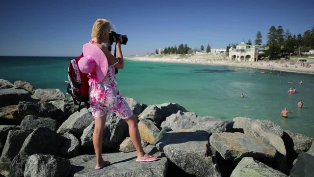 Woman photographer photographing the turquoise waters of Cottesloe Beach, Perth's most famous town beach, Western Australia. Indian Ocean in summer season with blue sky.