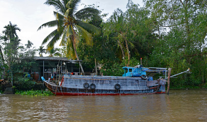 Fototapeta na wymiar An old wooden boat moored at the side of a waterway outside the city of Can Tho in the Vietnam Mekong Delta